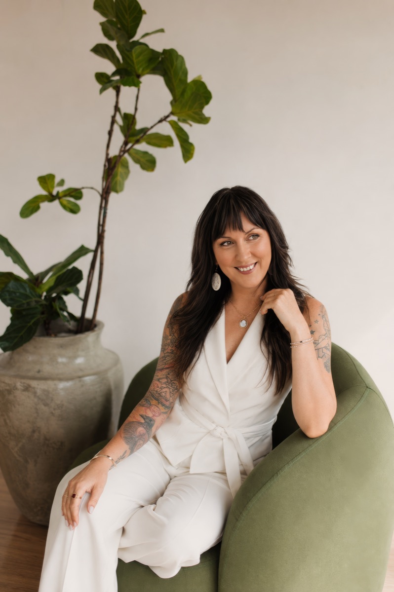 Erica Greye, founder of Restorative Living, seated in a green chair beside a fiddle leaf fig