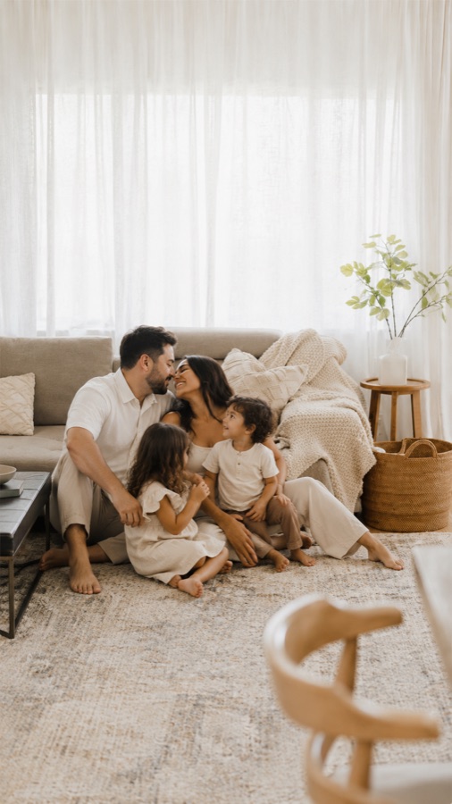 A family sitting together on the living room floor, warm natural light through sheer curtains